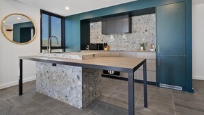 A modern kitchen with a central island, dark cabinetry, and a large window. - Spacious 2-Bed Apartment with Rooftop Views (North Fremantle)