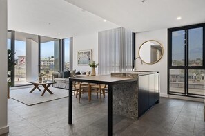 A modern living space with a kitchen island, dining area, and large windows offering city views. - Spacious 2-Bed Apartment with Rooftop Views (North Fremantle)