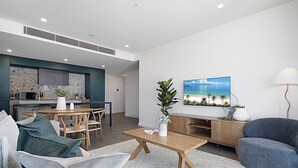 A modern living room with a wooden coffee table, a blue armchair, and a dining area with a kitchen in the background. - Spacious 2-Bed Apartment with Rooftop Views (North Fremantle)