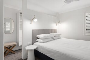 Ein Schlafzimmer mit einem Bett, Nachttischen, einem runden Spiegel und einem Deckenventilator.