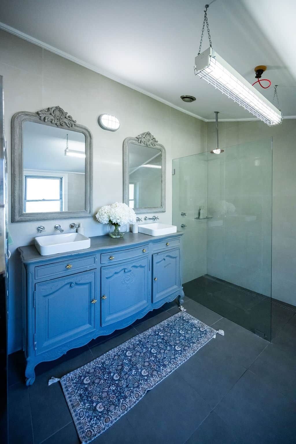 Un bagno con doppio lavabo, due specchi, una doccia e un tappeto a motivi.