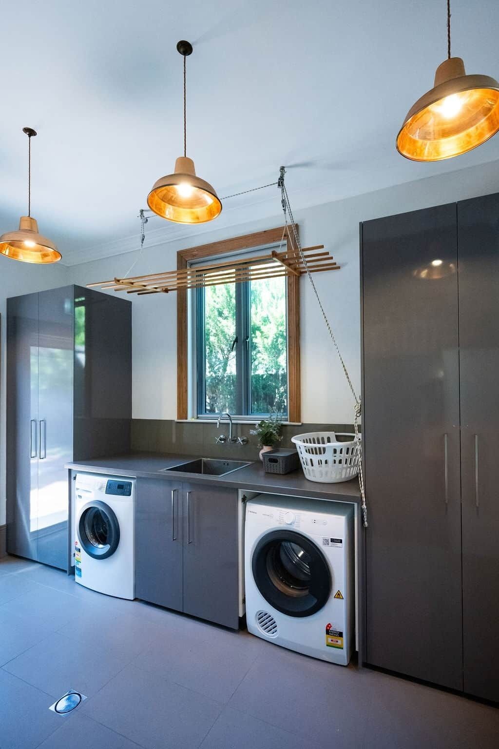 A modern laundry room with two washing machines, a sink, and wooden shelving.