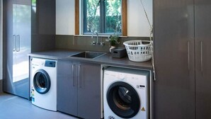 Une buanderie moderne équipée de deux machines à laver, d’un évier et d’étagères en bois.