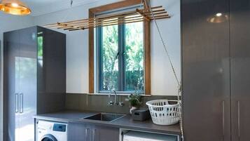 A modern laundry room with two washing machines, a sink, and wooden shelving.