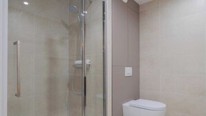 Un baño moderno con ducha envuelta en vidrio, inodoro blanco y barra de toallas de pared.