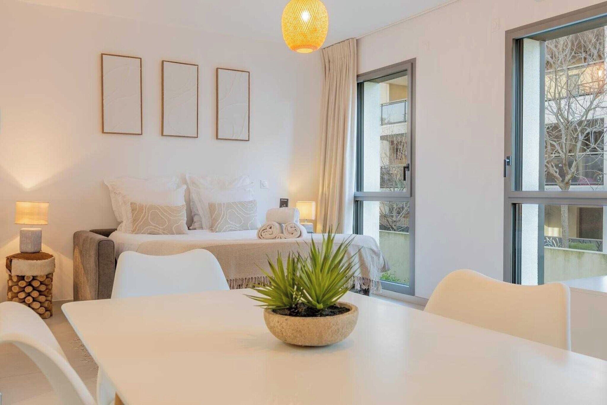 Habitación de hotel con cama, una mesa de comedor, una planta en maceta y ventana con vistas a árboles.