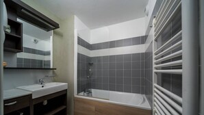 A bathroom with a sink, mirror, shower, and a built-in radiator. - C. du Verdon N°3307 - 2P6 (Allos)