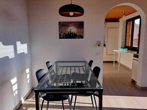 Un comedor con una mesa y sillas de vidrio, una lámpara colgante y un cuadro en la pared.