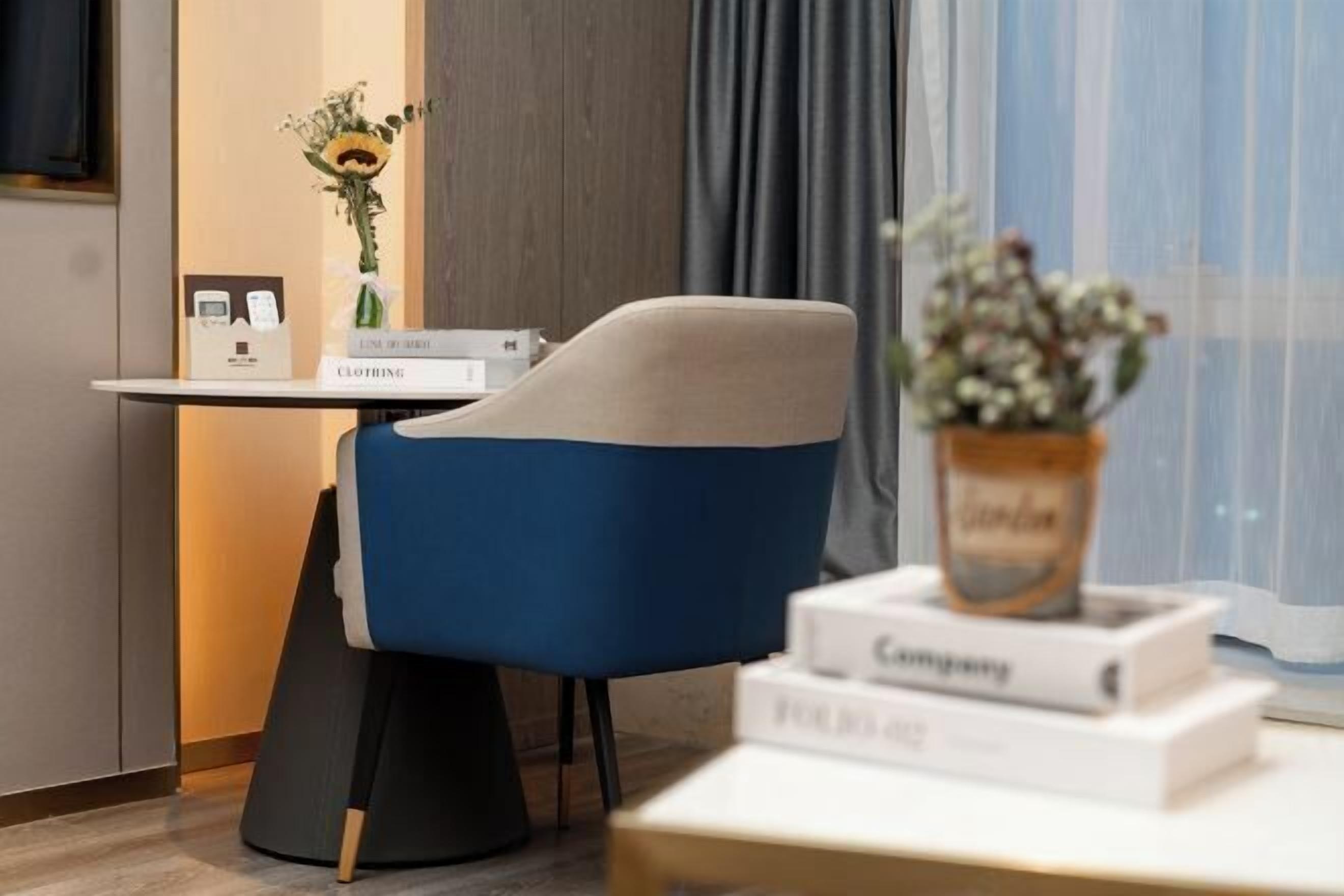A modern room with a blue chair, a small table with a vase of flowers, and a window with curtains.