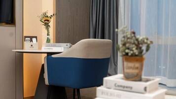A modern room with a blue chair, a small table with a vase of flowers, and a window with curtains.