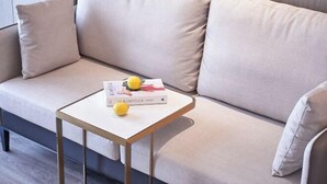 A sofa with cushions, a small table with a book and a yellow object, and a window in the background. - ECHARM PLUS Hotel (Guangzhou Dart International Center Changgang Metro Station) (Guangzhou)