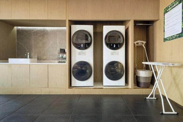 A modern laundry room with two front-loading washing machines, a sink, and a small table. - ECHARM PLUS Hotel (Guangzhou Dart International Center Changgang Metro Station) (Guangzhou)