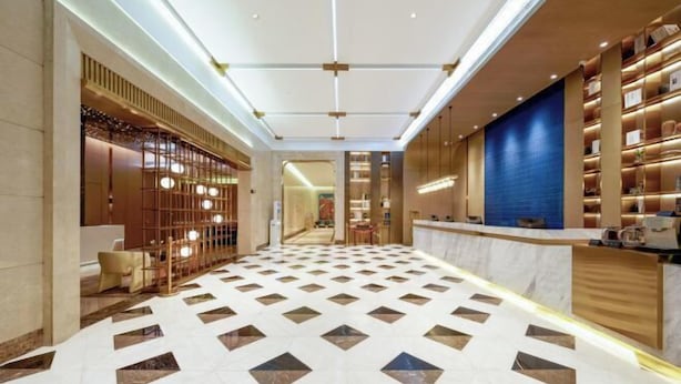 A hotel lobby with a geometric patterned floor, a reception desk, and a wall with shelves. - ECHARM PLUS Hotel (Guangzhou Dart International Center Changgang Metro Station) (Guangzhou)