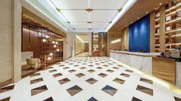 A hotel lobby with a geometric patterned floor, a reception desk, and a wall with shelves.