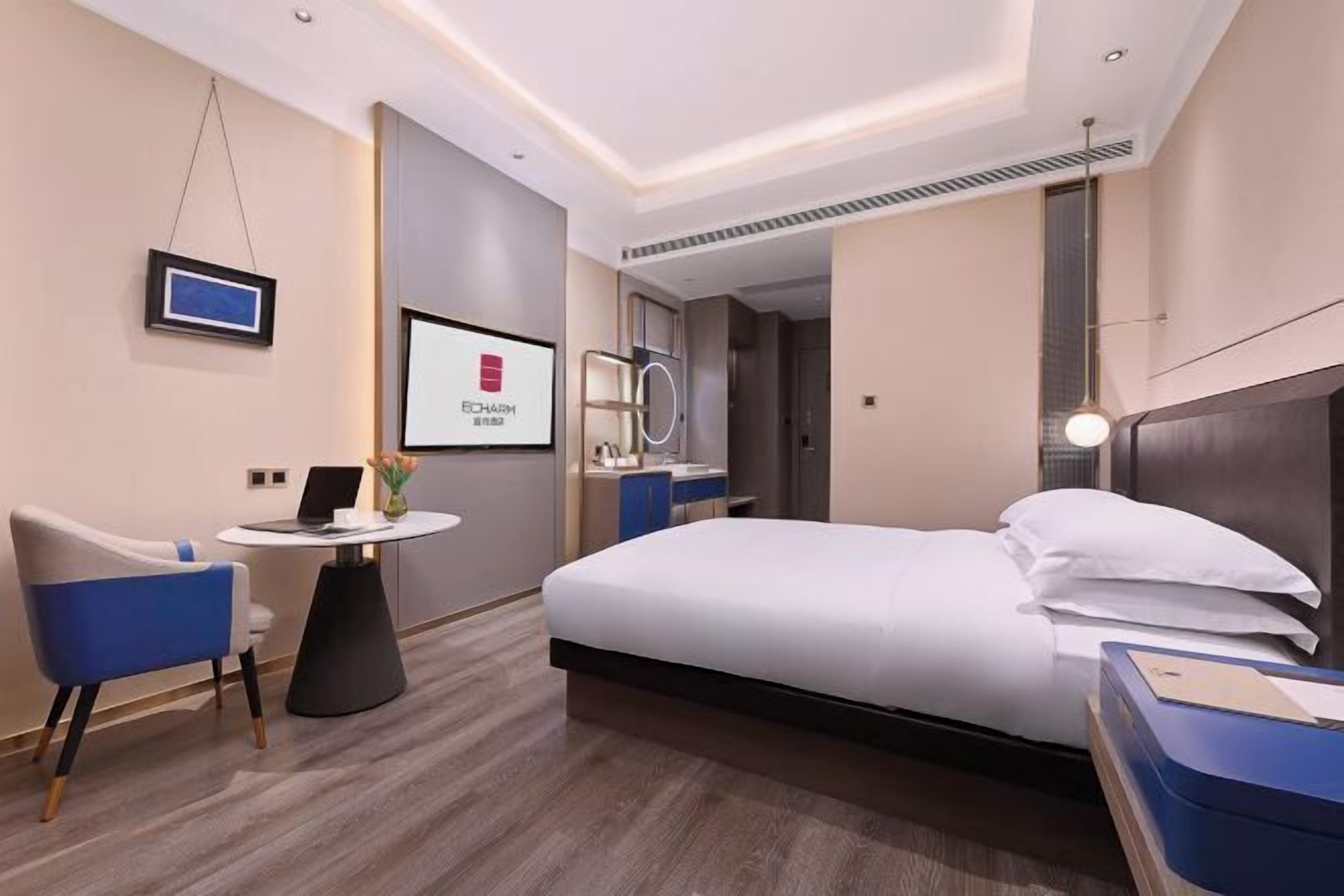 A modern hotel room with a bed, a desk, a chair, a TV, and a bathroom visible through an open door.