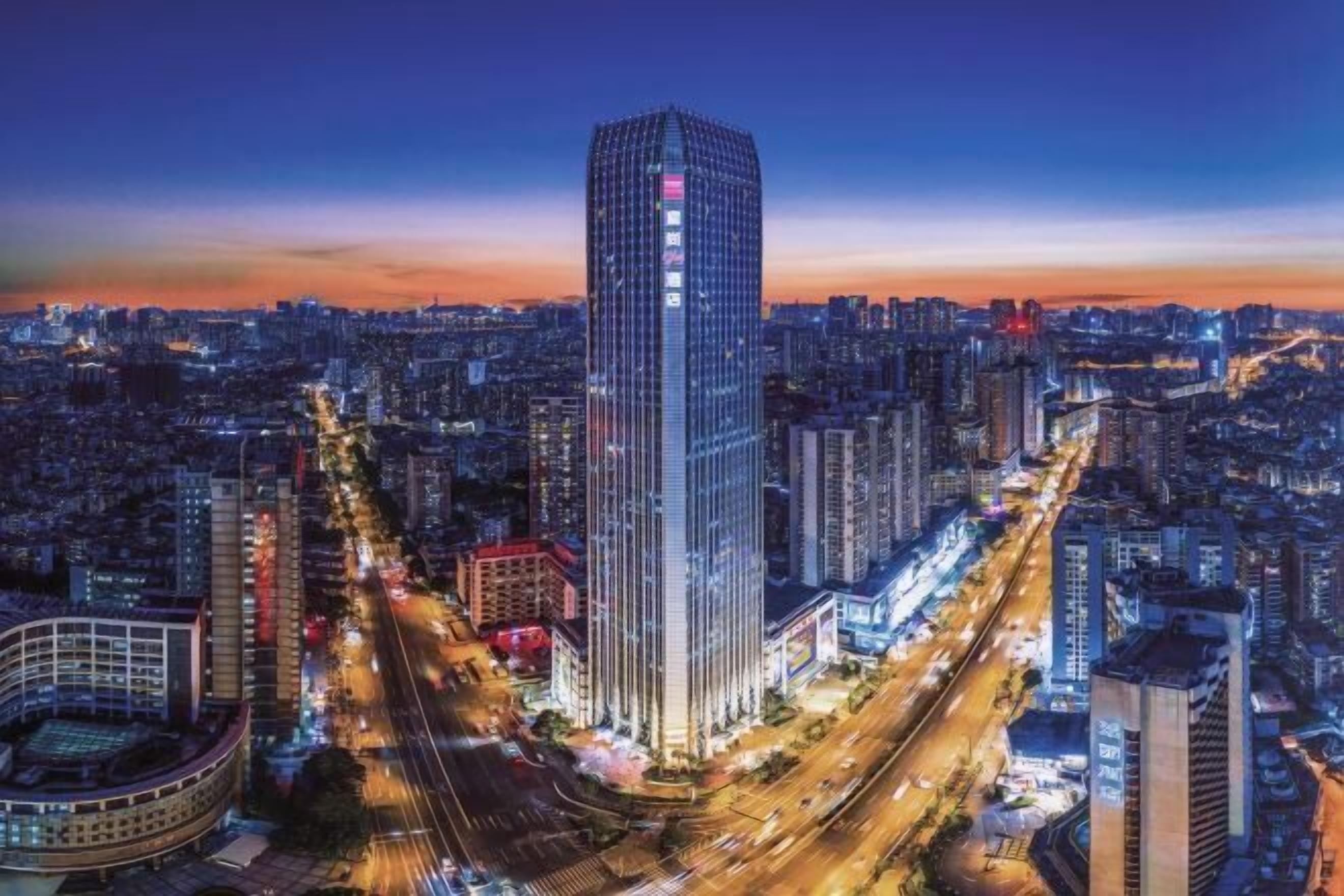 A high-rise building with a modern glass facade, surrounded by a dense urban environment with visible roads and other buildings.