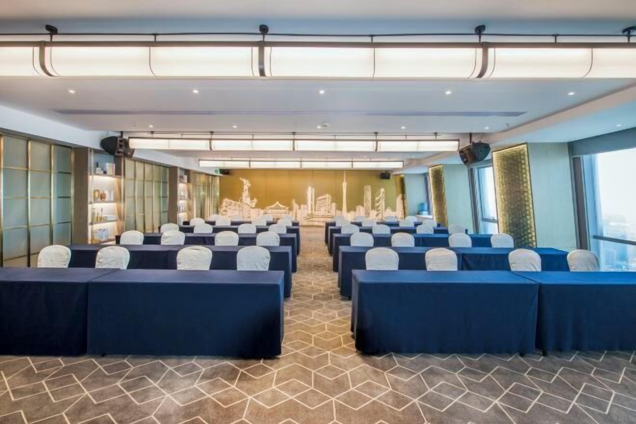 A conference room with rows of tables and chairs, a patterned carpet, and a cityscape mural on the back wall.
