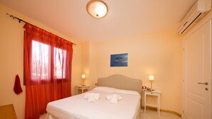 A hotel room with a bed, two bedside tables, a nightstand, a red curtain, a wall-mounted picture, and an air conditioning unit. - Ferienwohnung für 4 Personen in Imperia (Imperia)