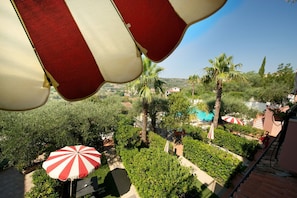 A view of a lush garden with palm trees and a pool area, with red and white striped umbrellas. - Ferienwohnung für 5 Personen in Imperia (Imperia)