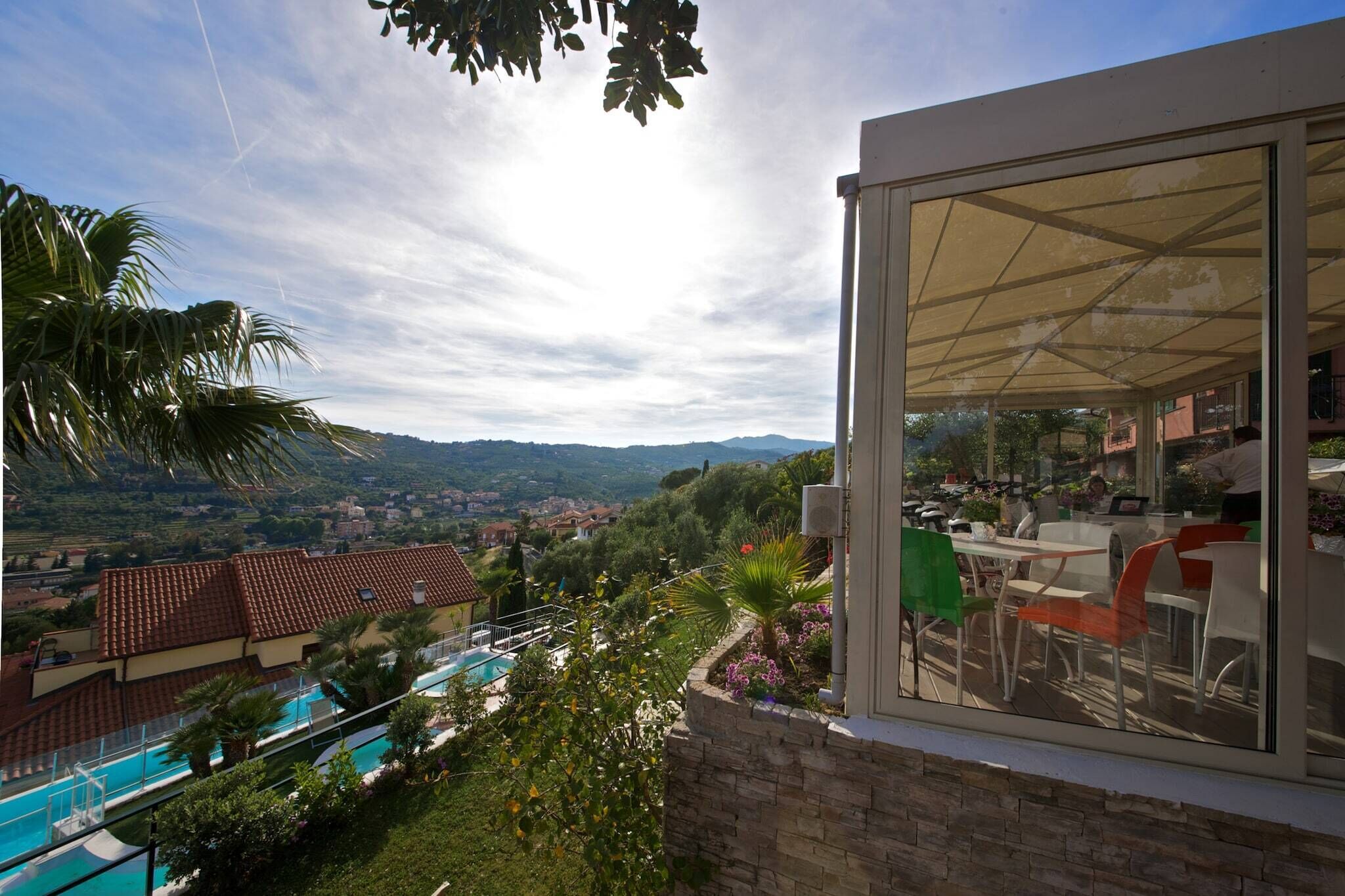 Ein moderner Außenbereich mit Sitzgelegenheiten, einer Glaskonstruktion, einem Pool und Blick auf eine hügelige Landschaft.