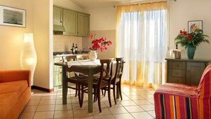 Uma sala de jantar com mesa e cadeiras, cozinha ao fundo e um sofá em primeiro plano.