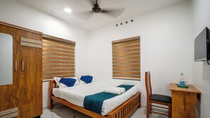 A bedroom with a bed, wooden wardrobe, desk, chair, and a television on the wall. - FORA INN (Kanayannur)