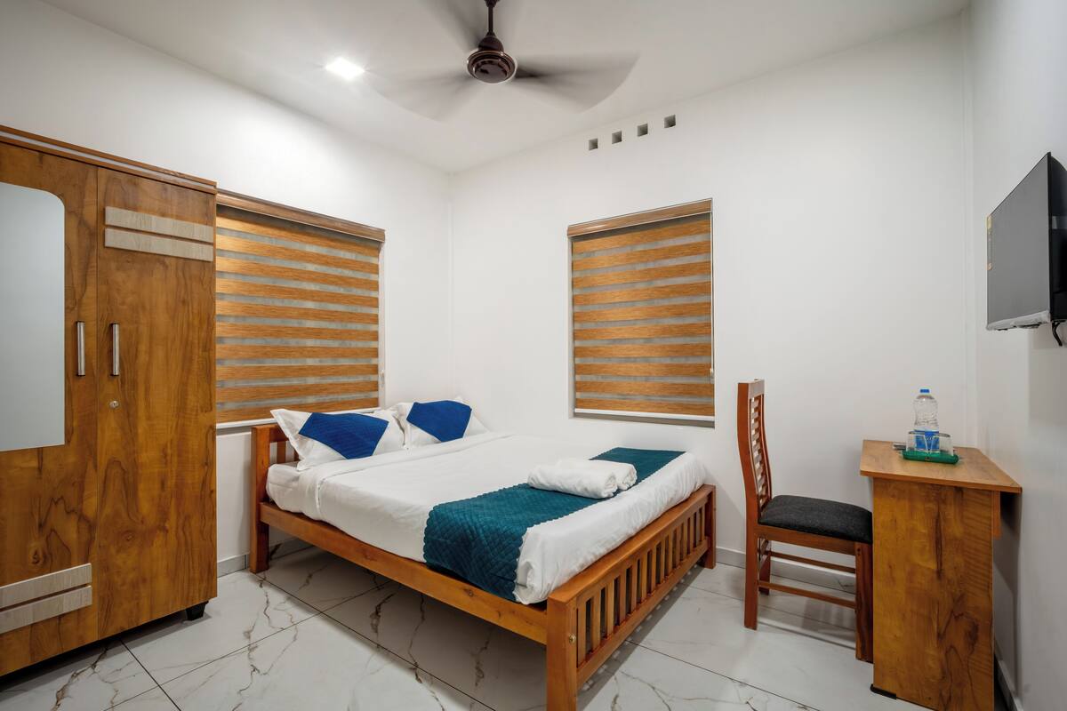 Ein Schlafzimmer mit Bett, Holzschrank, Schreibtisch, Stuhl und Fernseher an der Wand.