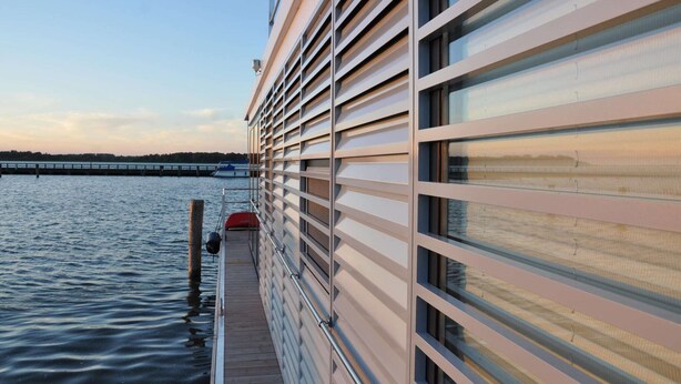 A waterfront building with a deck extending over the water, featuring large windows and a railing. - Hausboot Rosi mit Kajak in Ribnitz-Damgarten (Ribnitz-Damgarten)