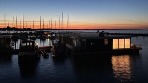 A marina at dusk with boats docked, a covered structure, and a distant shoreline. - Hausboot Rosi mit Kajak in Ribnitz-Damgarten (Ribnitz-Damgarten)