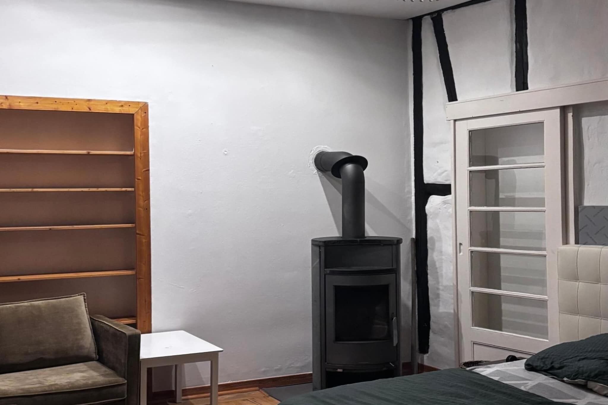 Una habitación con estante de madera, una mesita, una cama y un estufa de leña negra.
