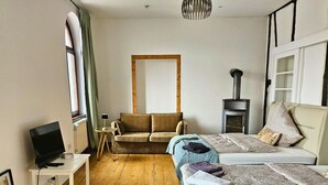 Quarto com duas camas, um sofá, televisão, mesa pequena, abajur e lareira.