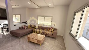 Een moderne woonkamer met een modulaire bank, een houten salontafel, en een eetgedeelte met stoelen.