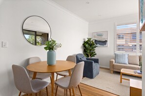 A modern living room with a round wooden table, grey upholstered chairs, a blue sofa, and a beige sofa. There is a large mirror on the wall, a potted plant, and a painting. - Bright 2-Bedroom Apartment Near Coogee Beach (Coogee)