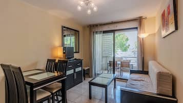 A modern living room with a glass dining table, black chairs, a sofa, a TV, and a ceiling light.