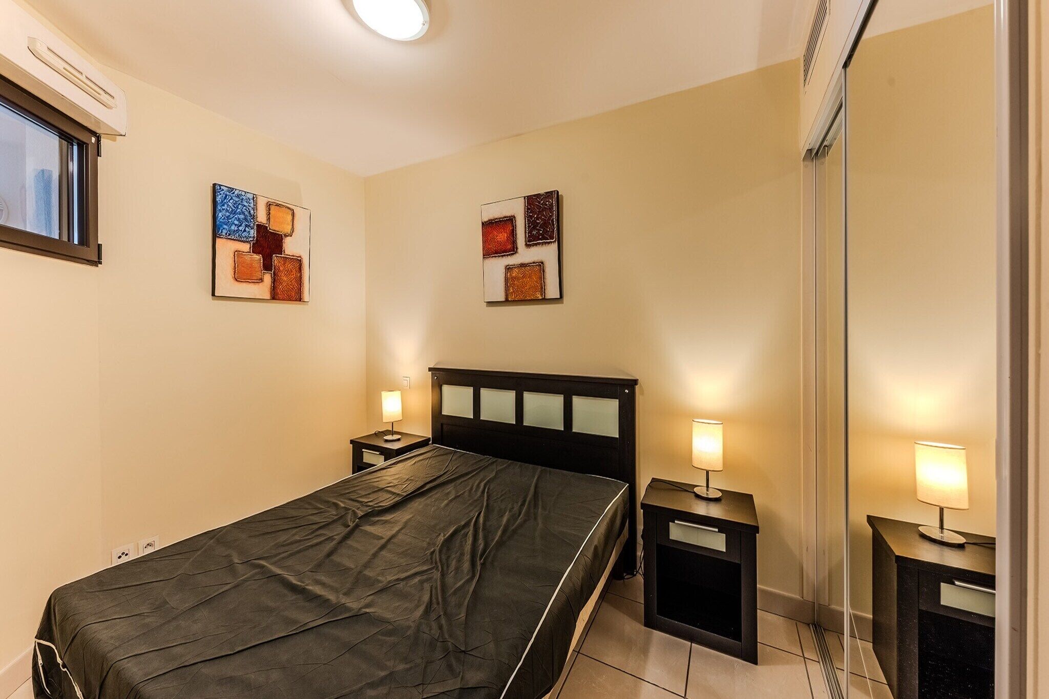 A hotel room with a bed, bedside tables, and wall art.