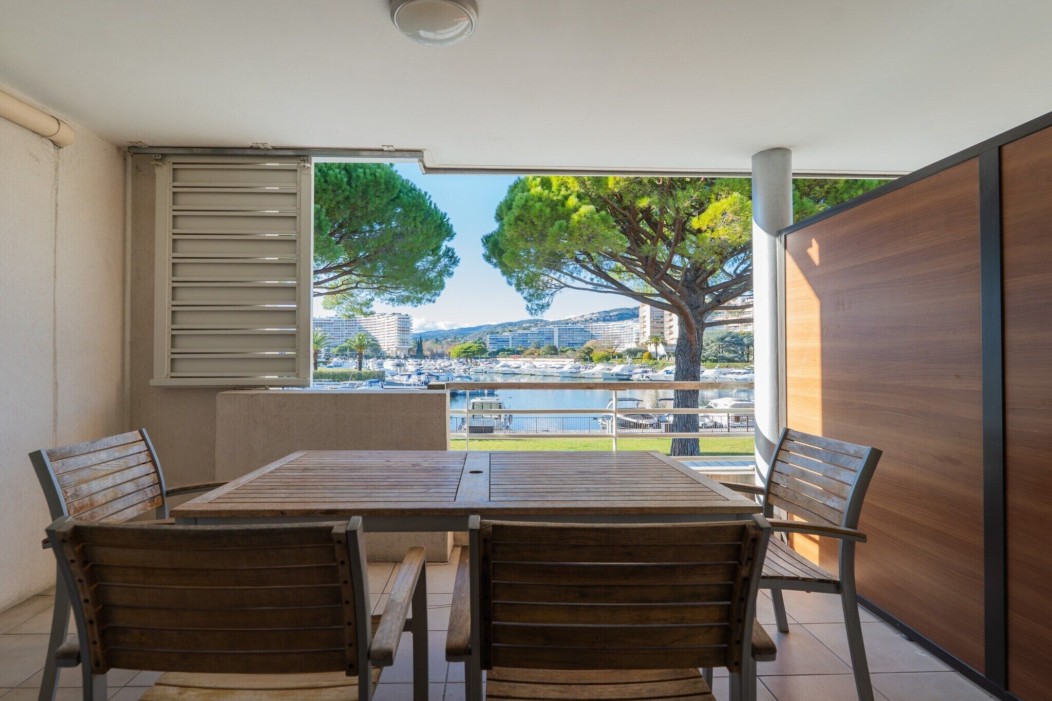 A balcony with a wooden table and chairs, a view of a marina, and a large tree.