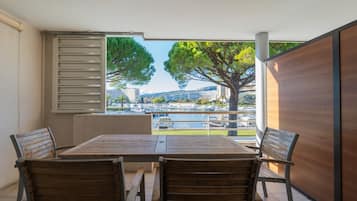 A balcony with a wooden table and chairs, a view of a marina, and a large tree.