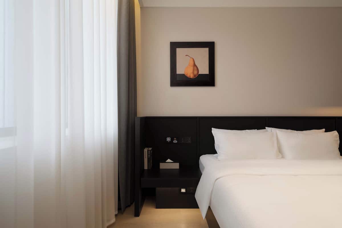 A hotel room with a bed, a nightstand, a framed picture, and a window with curtains.