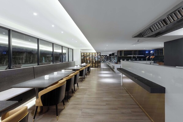 Un restaurant moderne avec de longues tables communes, un comptoir et une vue dégagée grâce à de grandes fenêtres.