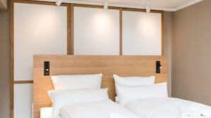 Hotellihuone, jossa on puinen päätyseinä, kaksi sänkyä ja seinään kiinnitetty valaisin.