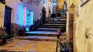 Une ruelle étroite avec des marches en pierre menant à un niveau supérieur. Des plantes en pot sont disposées le long des murs.