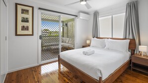 Quarto com cama de madeira, ventilador de teto, porta de correr de vidro que dá para uma varanda e um quadro pendurado na parede.