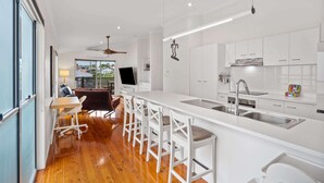Uma cozinha moderna com armários brancos, uma ilha central com banquetas, forno embutido e uma grande janela com vista para um jardim.