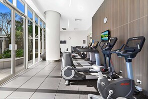 A gym with cardio machines and a TV screen on the wall. - Stylish 2-Bed Apartment in Surfers Paradise (Surfers Paradise)