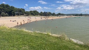 Uma praia com pessoas tomando sol e nadando, uma área gramada em primeiro plano e um edifício ao fundo.
