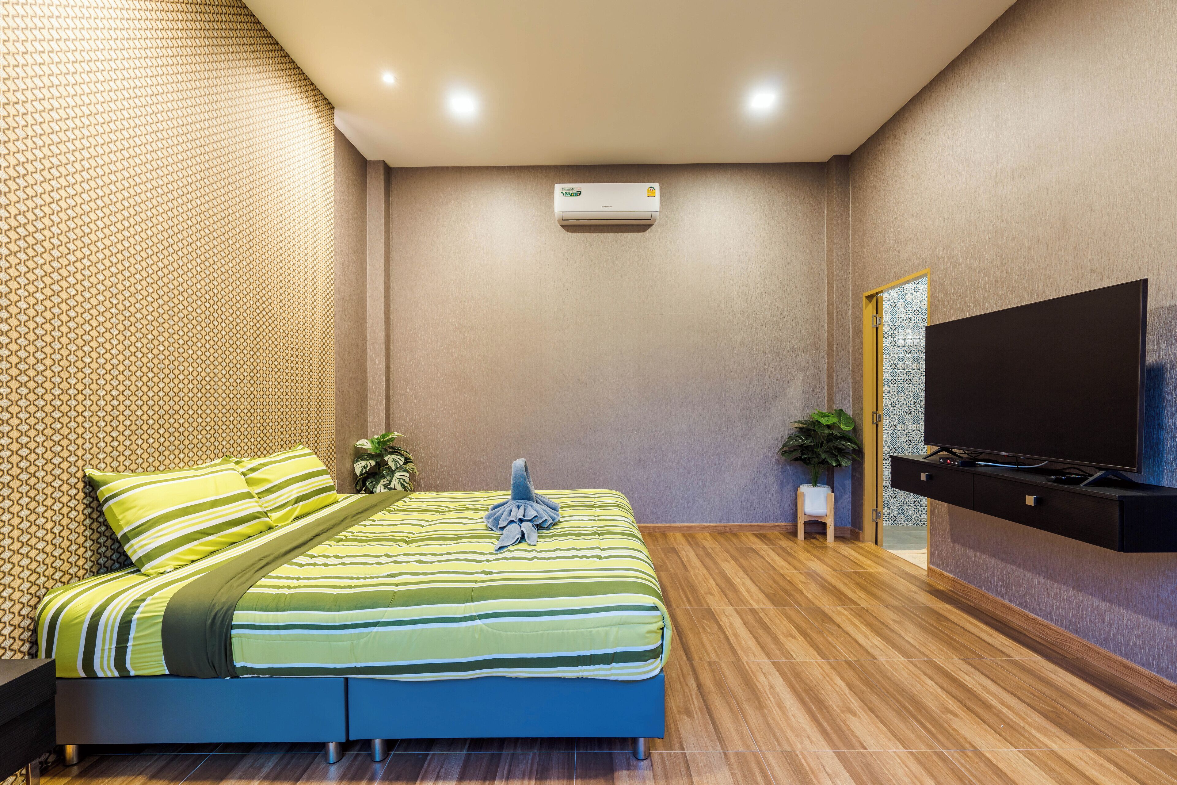 A modern hotel room with a bed, a flat-screen TV, an air conditioning unit, and a wooden floor.