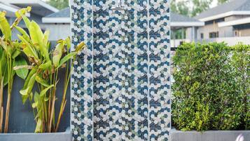 Una pared de azulejos con un diseño geométrico, una planta en maceta de hojas anchas y un seto bien recortado.