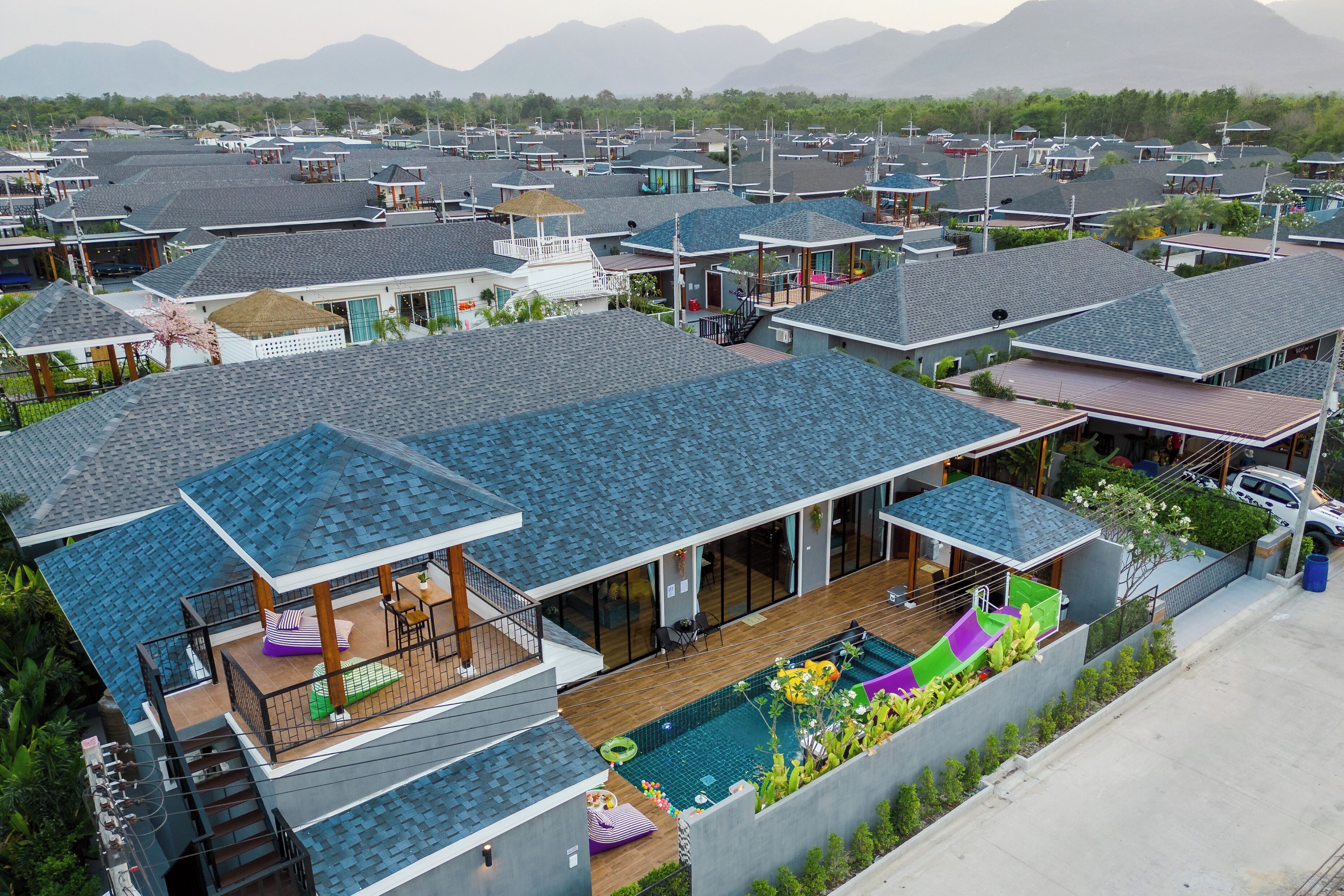 Zona residencial con varias casas de arquitectura moderna, piscina y vistas a montañas al fondo.