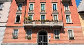 Un edificio a più piani con facciata rossa, numerose finestre e un ingresso centrale con cancello in metallo.