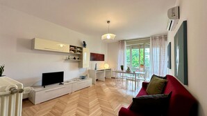 Una sala de estar moderna con televisión, mueble blanco para entretenimiento, mesa de comedor y sofá rojo.